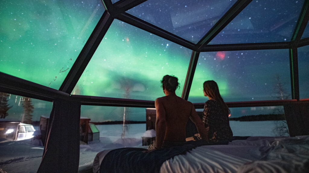 coppia che guarda l'aurora boreale da un igloo trasparente in Finlandia